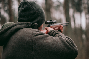 Man with a green beanie holding a rifle during a fall hunt.