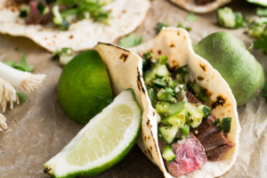 Elk meat tacos with green salsa on top. A lime edge is next to the taco