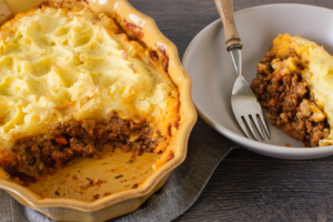 shepherd's pie in a yellow baking dish with a scoop of it on a plate with a fork.